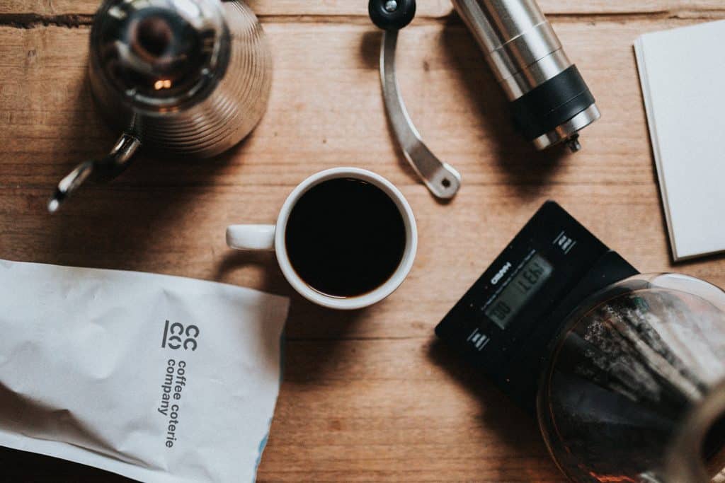 Electric coffee percolator, coffee cup, and grinder on table
