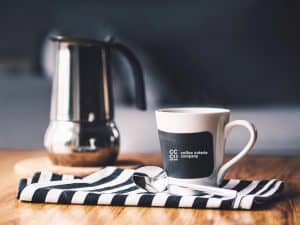 Stainless steel moka pot and coffee coterie cup on wooden table
