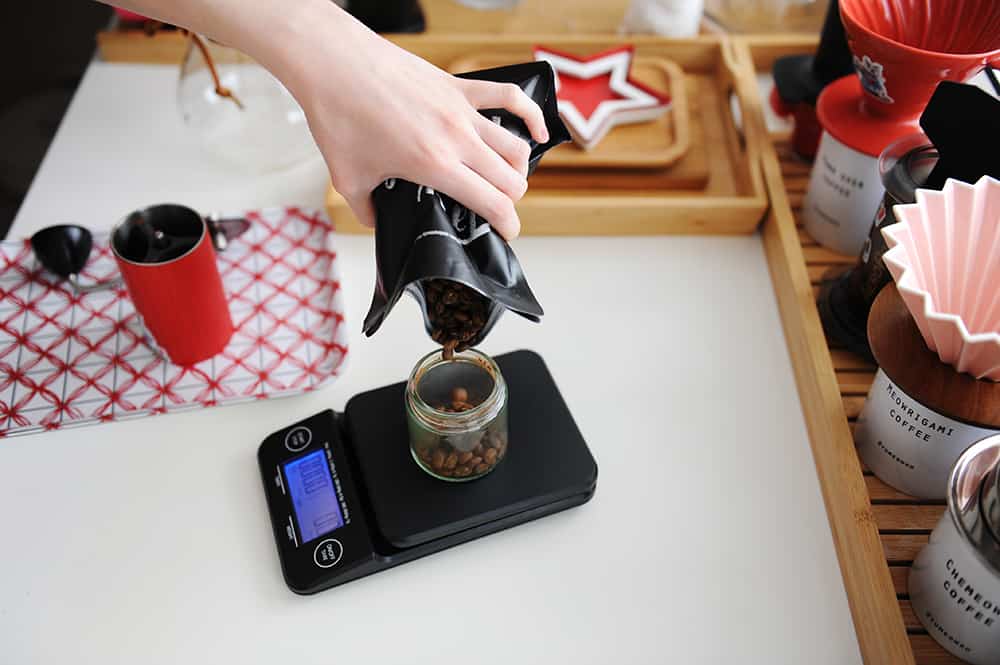 CoffeeWaterRatio Scale Coffee To Water Ratio - Pour coffee beans into red manual grinder on electronic scale.